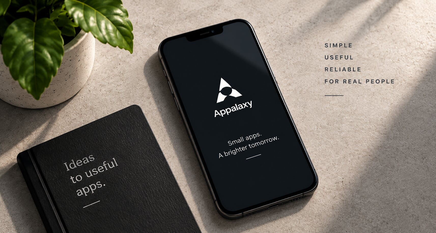 A phone showing the Appalaxy splash screen next to a notebook reading 'Ideas to useful apps.' on a desk with a plant